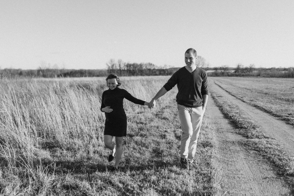 Couple walking alongside tall grass field holding hands