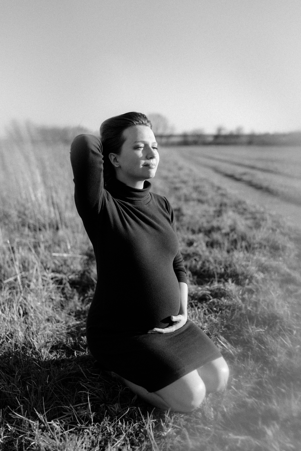Pregnant woman sitting in field holding belly