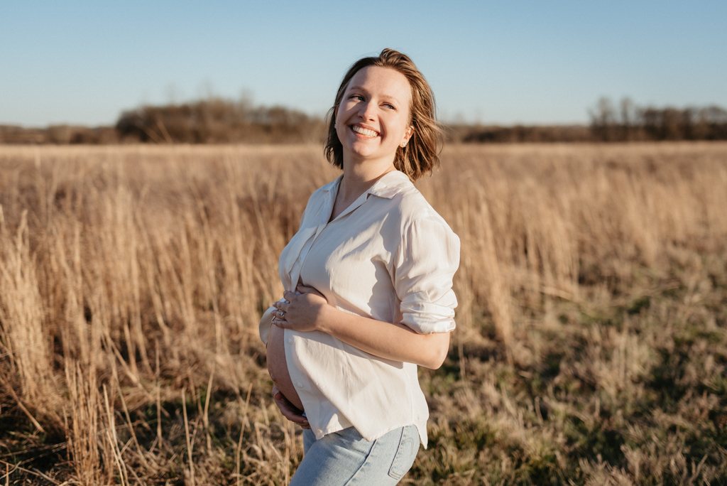 Pregnant woman smiling in field holding belly