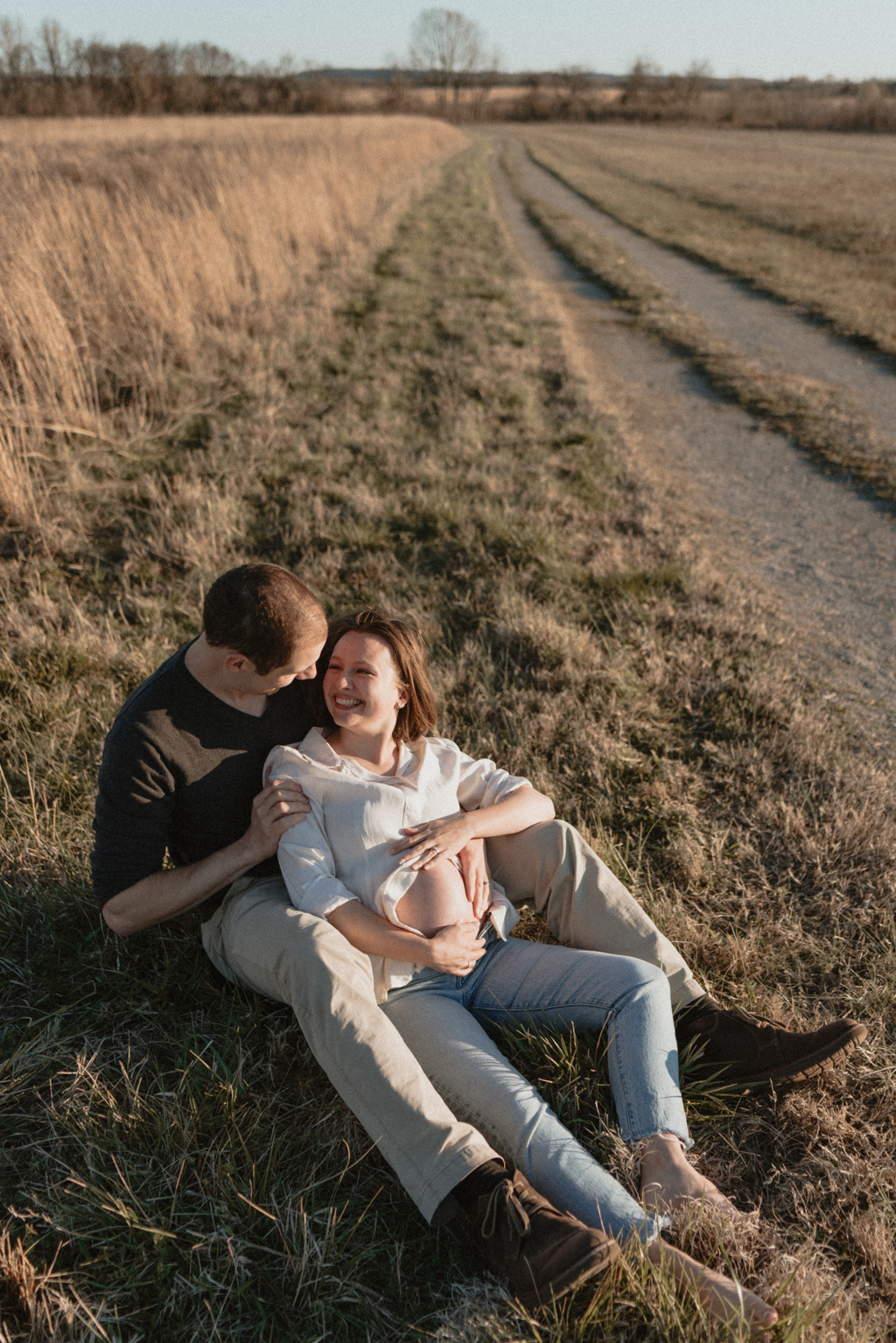 Couple smiling in field while rubbing pregnant belly
