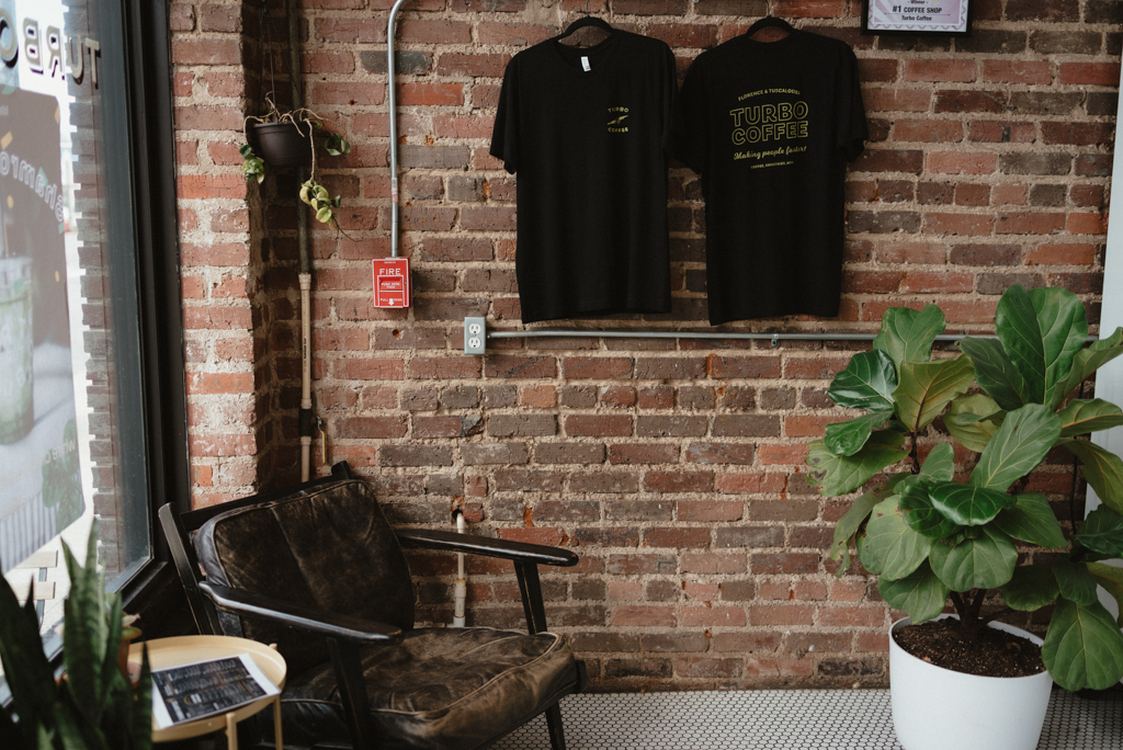 Two shirts hanging up at coffee shop against brick wall
