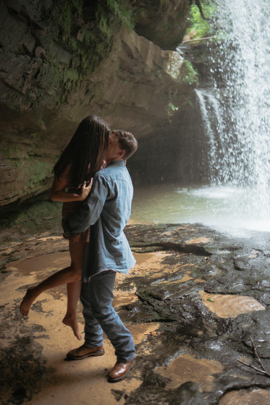 Man holding up woman underneath waterfall