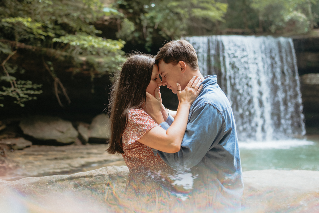 Man and woman holding each others faces in front of waterfall