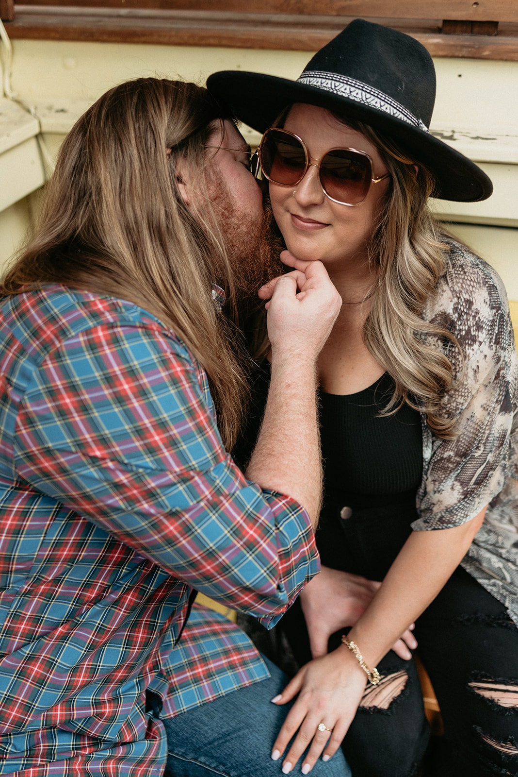 Woman sitting with sunglasses on while man kisses her cheek