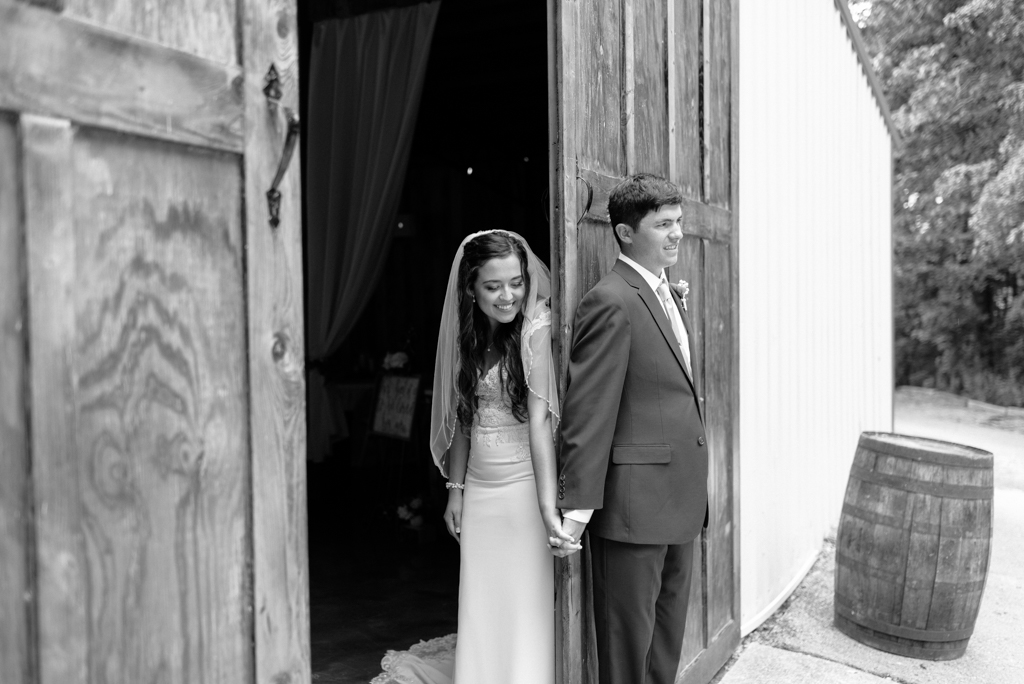 Bride and groom holding hands behind barn door